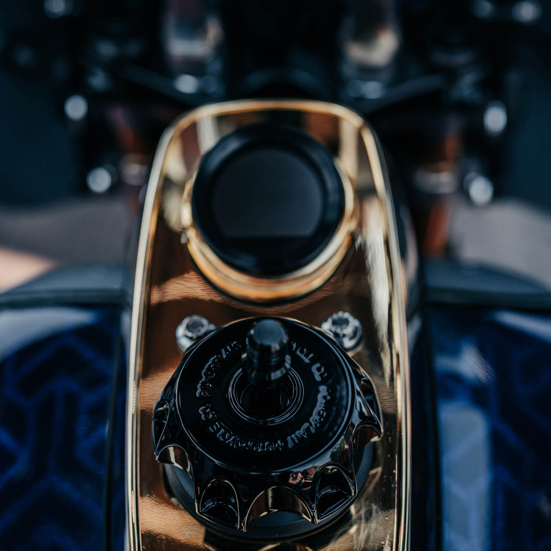 Gold plated Harley FXR dash with black moto style gas cap and black Koso digital fuel gauge on gas tank with blue and black Escher pattern paint job.